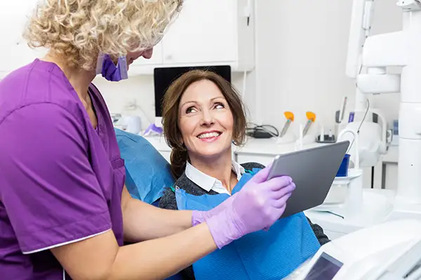 A smiling female patient interacting with her dentist, who is holding a tablet to explain her dental examination results. A smiling female patient interacting with her dentist, who is holding a tablet to explain her dental examination results.