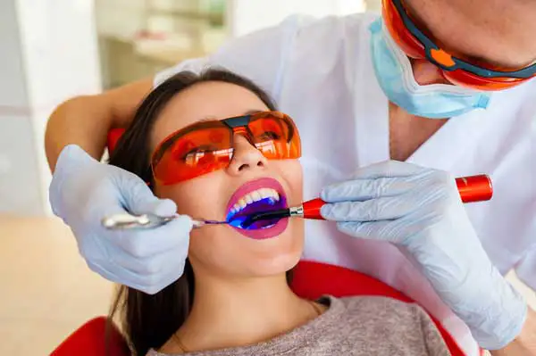 A dentist using a blue curing light to harden a filling while the patient wears protective glasses, highlighting the modern dental filling process. A dentist using a blue curing light to harden a filling while the patient wears protective glasses, highlighting the modern dental filling process.