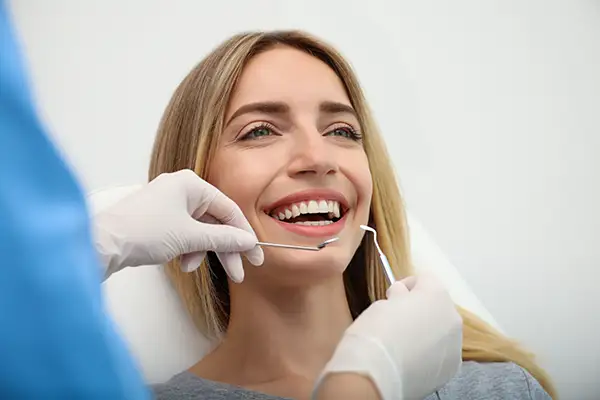A female patient smiling during a routine dental checkup as a dentist uses dental tools to examine her teeth. A female patient smiling during a routine dental checkup as a dentist uses dental tools to examine her teeth.