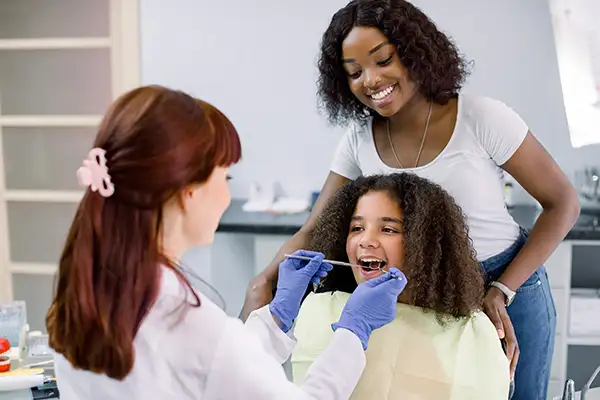 A pediatric dentist examines a calm girl's mouth while her mother watches during a routine dental checkup. A pediatric dentist examines a calm girl's mouth while her mother watches during a routine dental checkup.