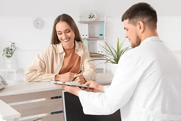 Female patient at a dental office reception desk filling out new patient forms while being assisted by a staff member. Female patient at a dental office reception desk filling out new patient forms while being assisted by a staff member.