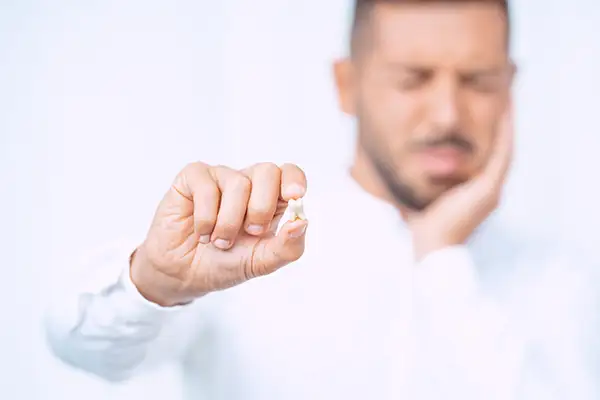 A man holding a wisdom tooth after extraction, wincing and holding his jaw due to impacted wisdom tooth discomfort. A man holding a wisdom tooth after extraction, wincing and holding his jaw due to impacted wisdom tooth discomfort.